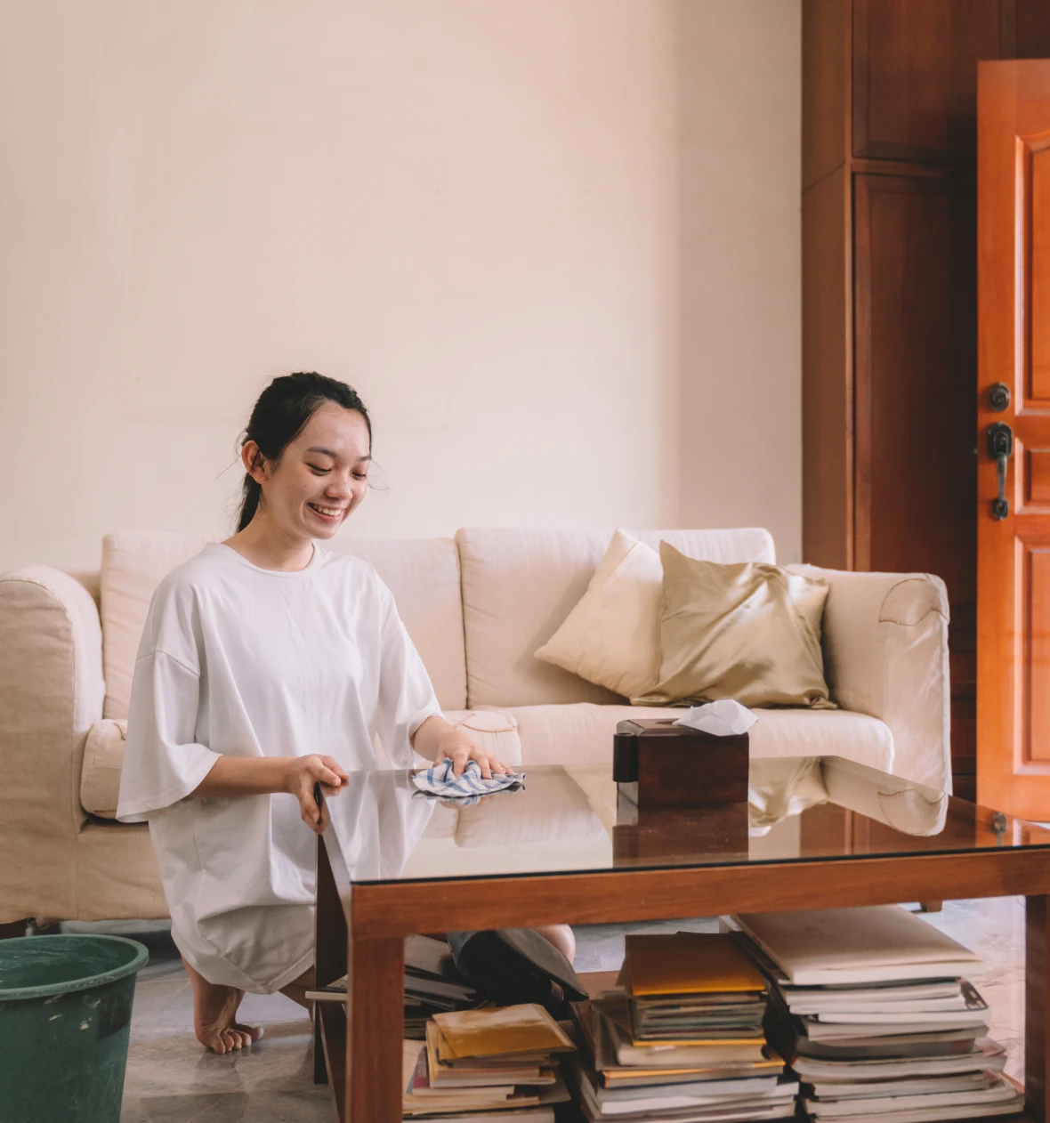 Woman cleaning glass coffee table, smiling.