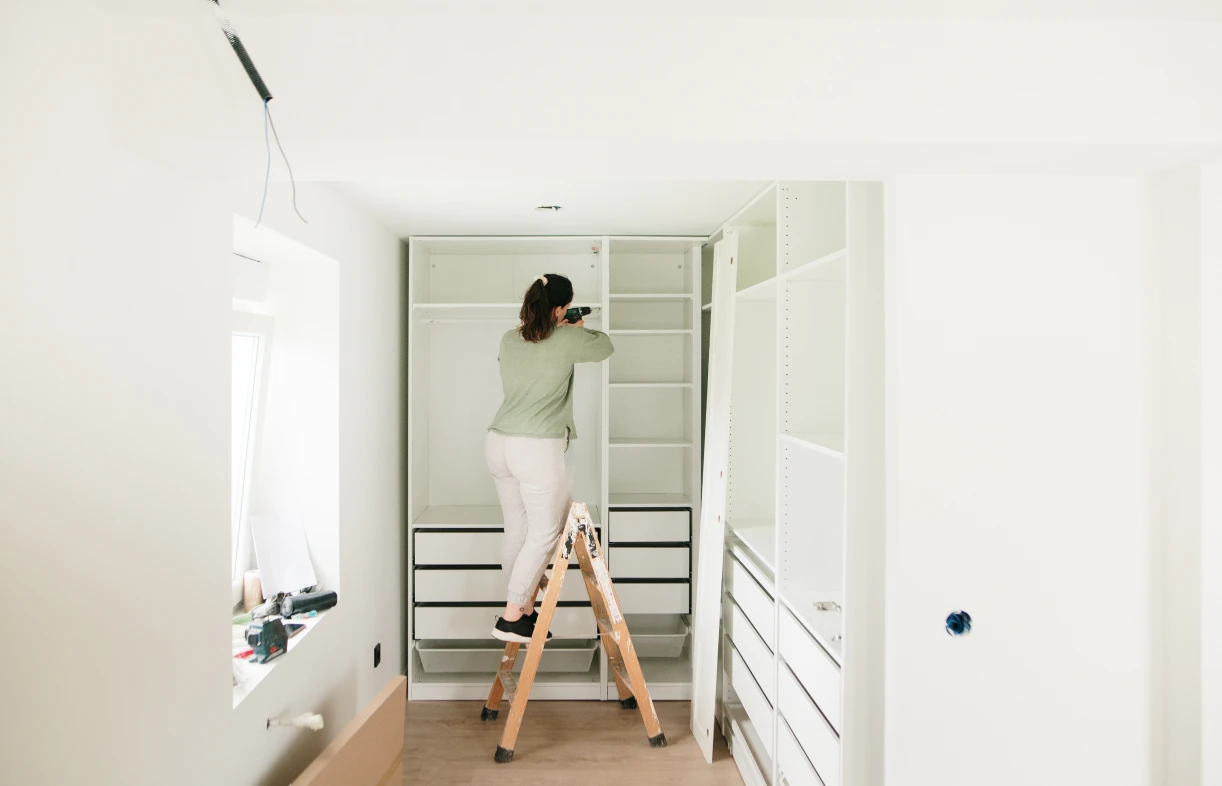 Person assembling closet on a small ladder.